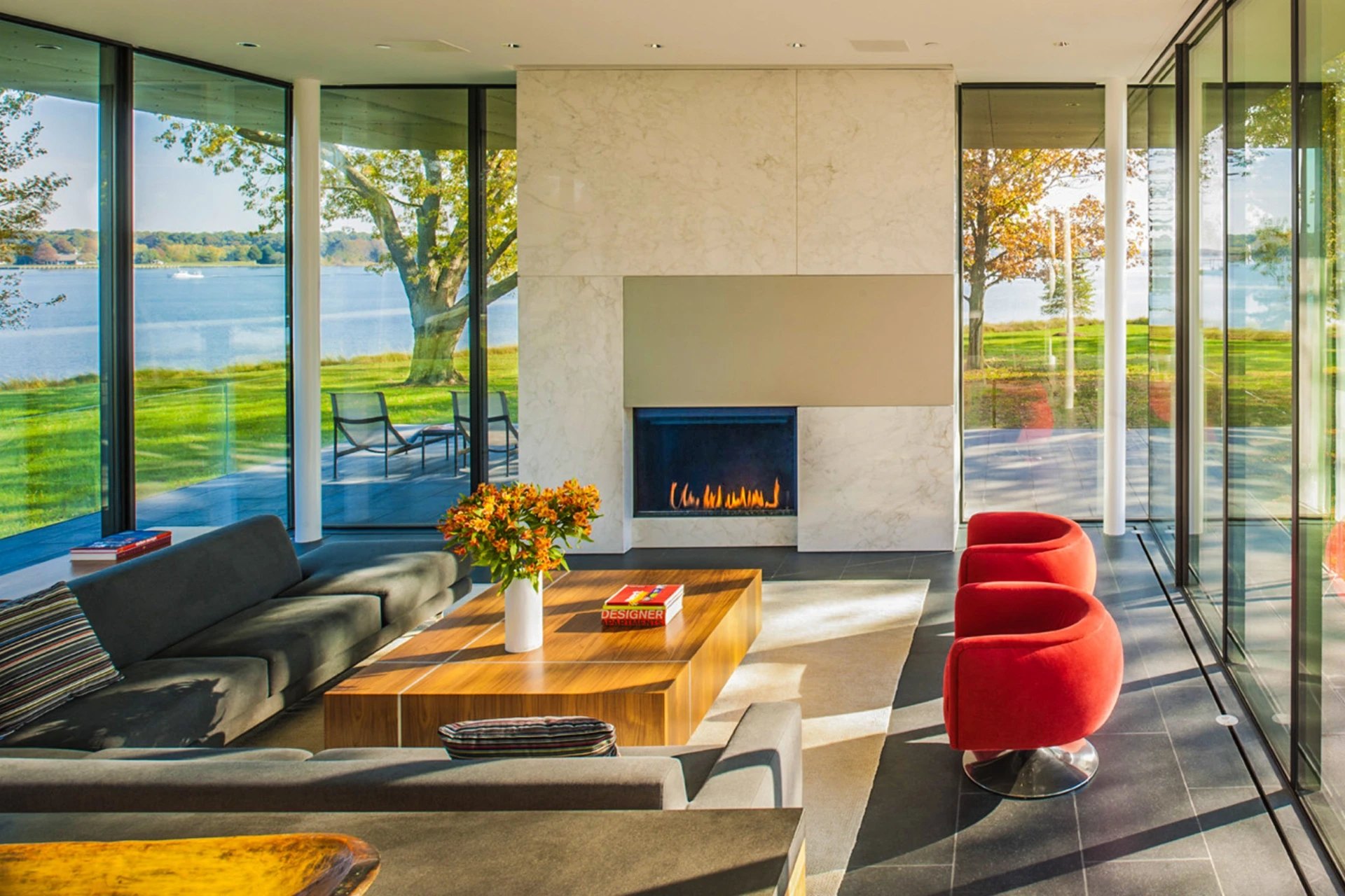 Glass-walled waterfront living room with marble fireplace and lake views
